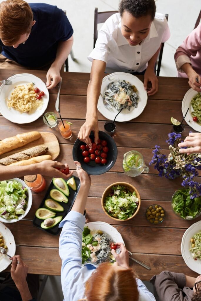 pexels-photo-3184188-3184188 A group of people sharing a vibrant meal with salads, pasta, and fresh vegetables, promoting togetherness.